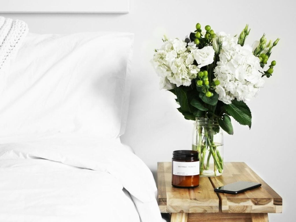 A Beautiful Flowers inside a Minimalistic Vase on top of Jute Bedside Table
