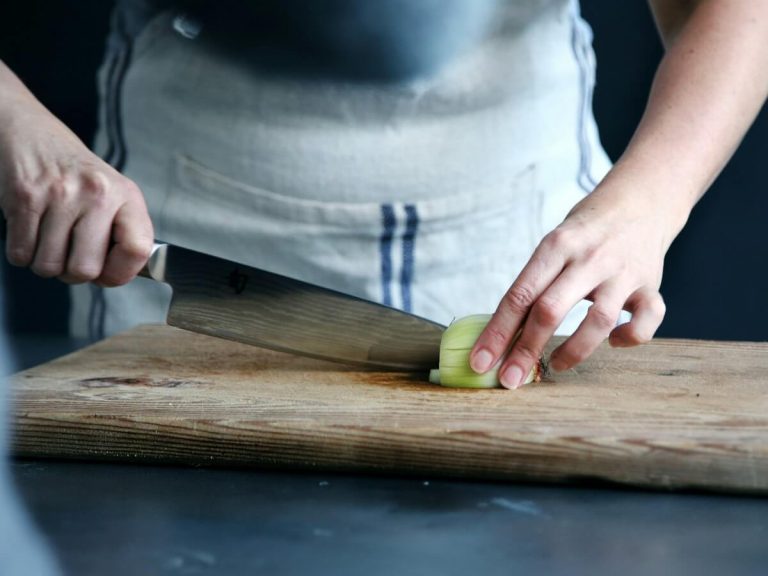 Close-up of hands chopping an onion on a wooden board—highlighting efficient meal prep in a modern kitchen