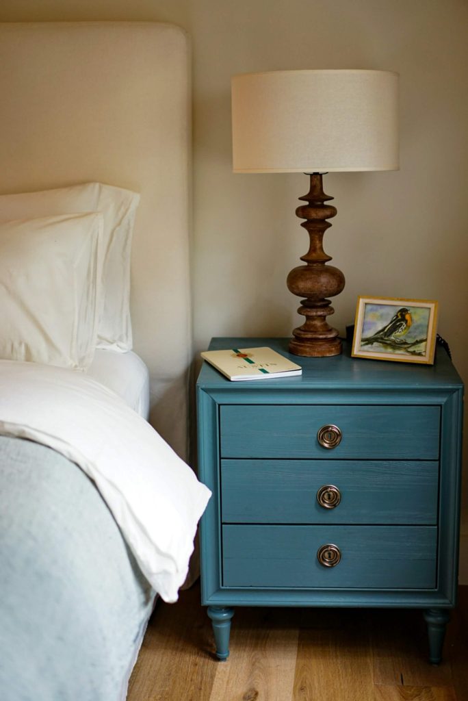 A brown wooden nightstand next to a queen bed by Megan Bucknall