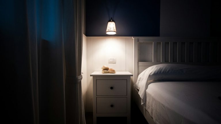 A minimalist white nightstand next to a double bed by Lu