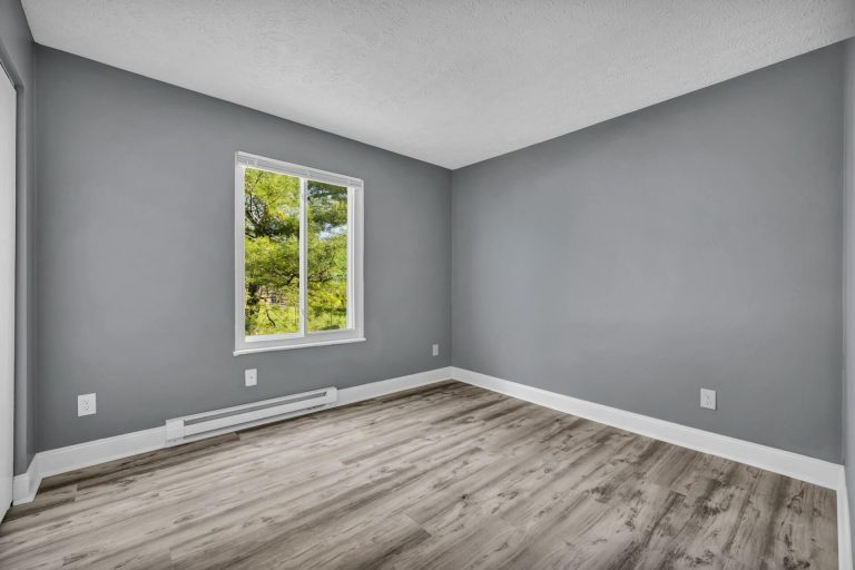An apartment bedroom with gray walls and a single window by Josh Lemmon